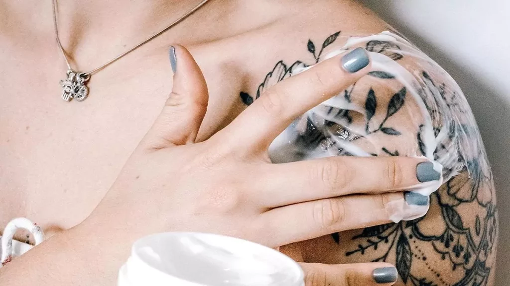 Mulher aplicando pomada para cicatrizar tatuagem no ombro